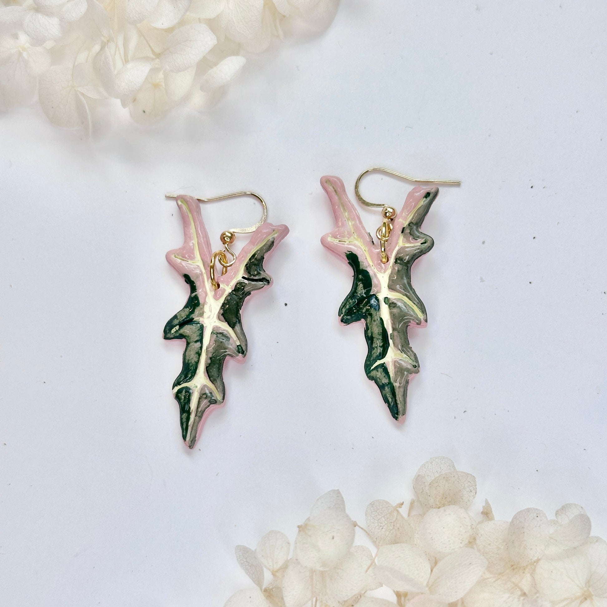 Pair of leaf-shaped earrings on a white background with decorative stones.