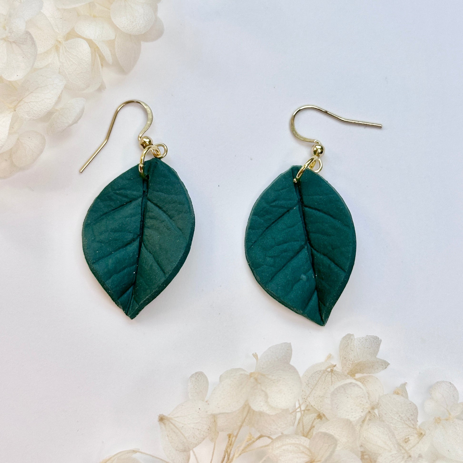 Green leaf-shaped earrings on a white background with white flowers.