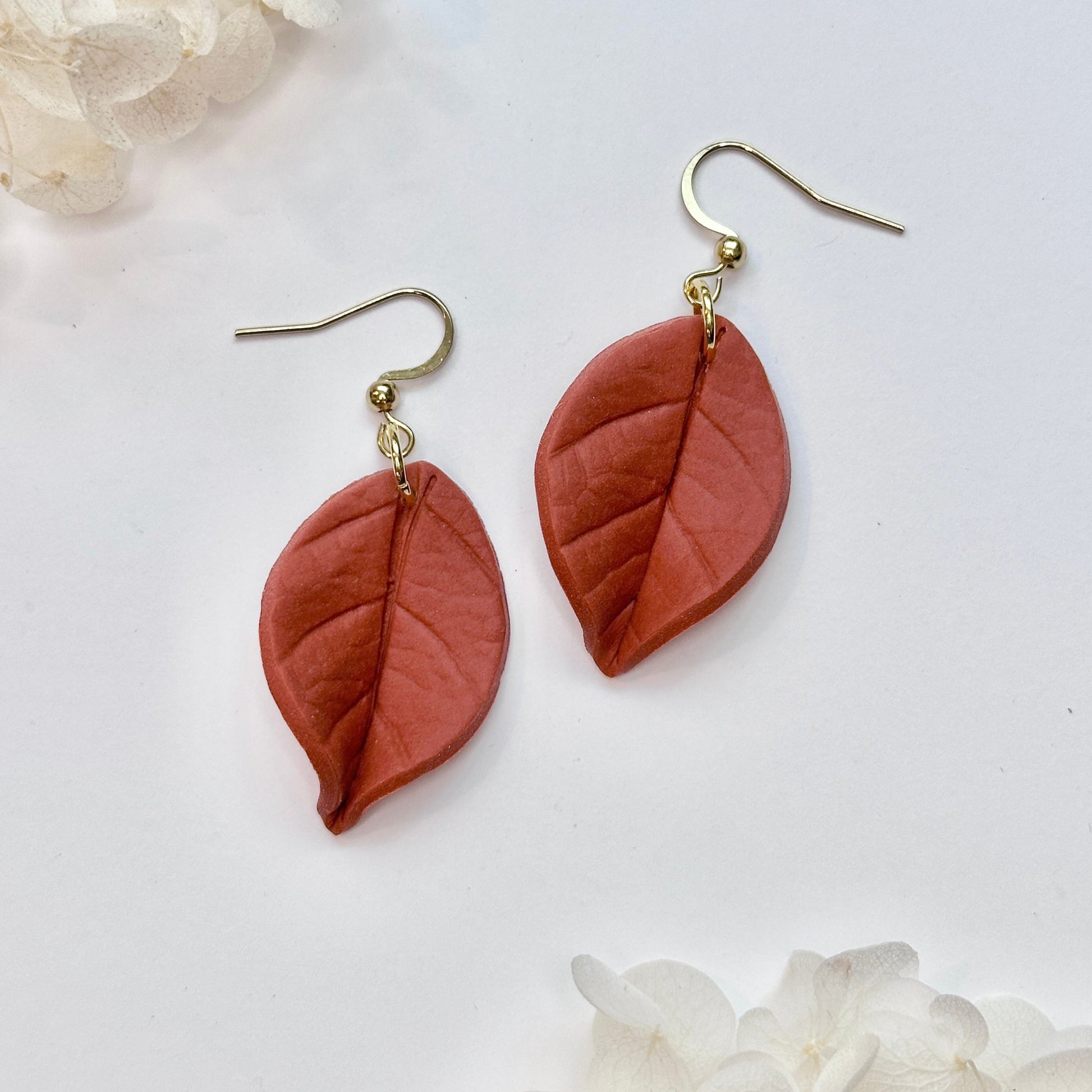 Pair of leaf-shaped earrings on a white background with floral elements.