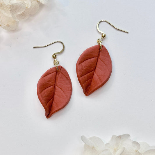 Pair of leaf-shaped earrings on a white background with floral elements.