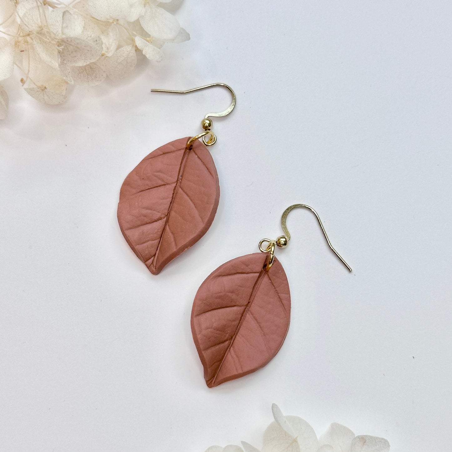 Pair of leaf-shaped earrings on a white background with floral elements.